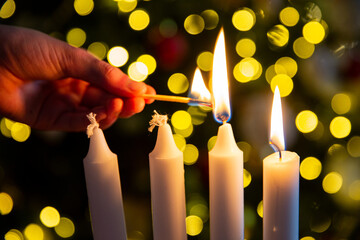 Hand lighting second candle with a match on Advent wreath with four pillar candles. Christmas tree...