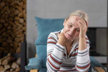 Middle-aged woman resting her head on her hand, sitting indoors with a thoughtful and serene...