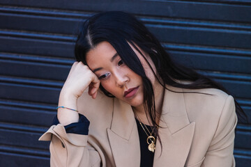 Sad and depressed young asian businesswoman leaning against closed garage door with hand on face