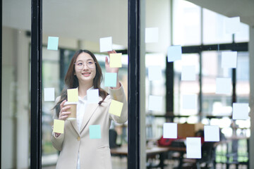 Businesswoman writing on sticky notes while planning business strategy