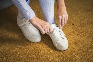 Person tying laces of stylish white sneakers on carpet
