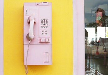 Vintage Payphone pink pastel color installed on yellow wall.