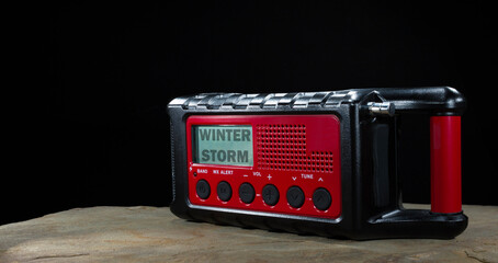 Winter storm watch showing on a weather radio that has a battery backup with small solar panel and a hand crank on a black background.