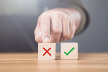 A man choosing between a checkmark and an 'X' symbol on wooden blocks. Image represents the concept of making the right choice, highlighting the importance of distinguishing between right and wrong