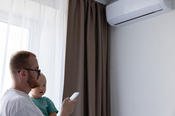 Father and little son turn on air conditioner using remote control.