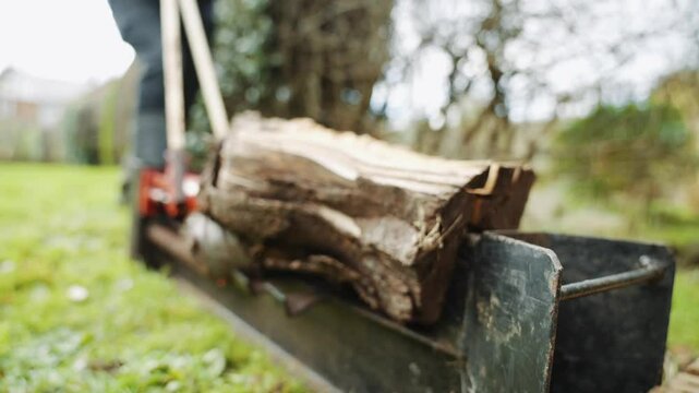A man is using a log splitter to split a log. The splitter is black and the log is brown