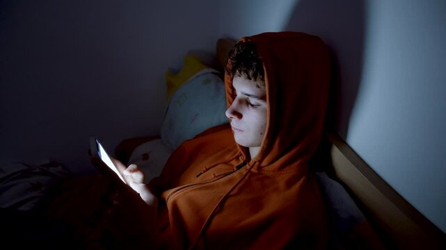 4k medium handheld shot of teenager using a smartphone lying in bed late at night, playing games, watching videos, and scrolling the screen.Children's screen addiction.Screen Addiction in Youth