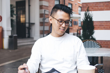 Fototapeta premium Adult ethnic man using smartphone while sitting at table with notepad and to go beverage on cafe terrace