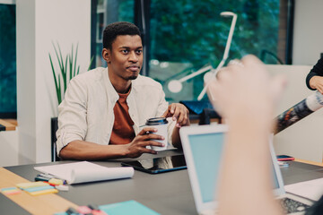 Fototapeta premium Group of smart casual male and female colleagues collaborating near table desktop in modern coworking space, diversity millennial students brainstorming on information for university project