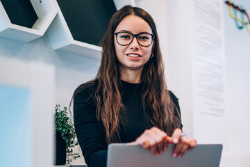 Attractive female graphic designer in optical spectacles smiling at camera during time for distance...