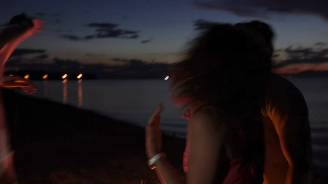Group of friends dancing around fire on the beach