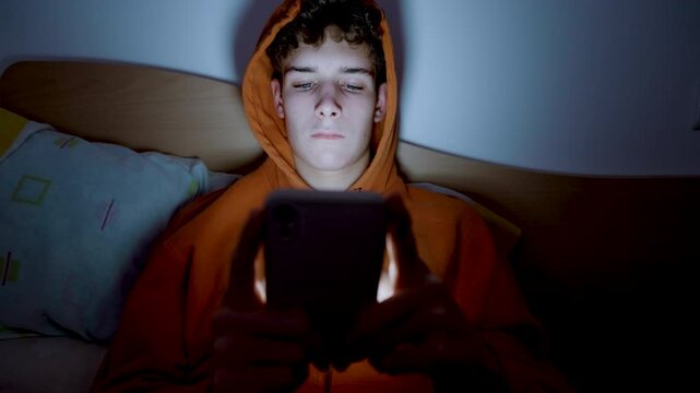 4k medium handheld shot of teenager using a smartphone lying in bed late at night, playing games, watching videos, and scrolling the screen.Children's screen addiction.Screen Addiction in Youth