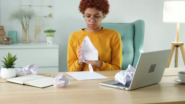 Start up business concept. Sad african business woman writing document crumpled paper and tossed it. Proposed project failed. Tired overworked girl no idea sitting at workplace writing notes at office