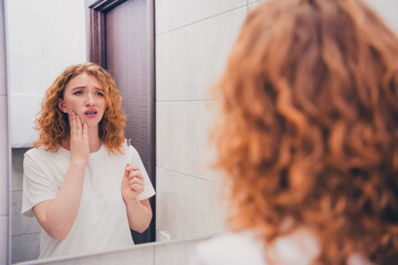 Photo of young woman brushing teeth suffering pain toothache looking in mirror in bathroom morning...