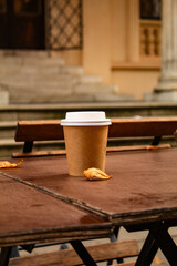 Coffee in a gray cup, with a white plastic lid on a wooden table in an empty cafe, in autumn