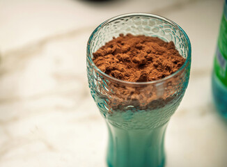Glass of milk topped with cocoa powder, ready for mixing to create a chocolate milk drink. Close-up view on a marble surface.