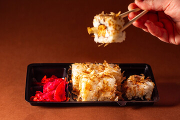 Chopsticks taking portion of sushi roll. Sushi rolls with salmon cream cheese and cucumber in take away packege. Food delivery concept.