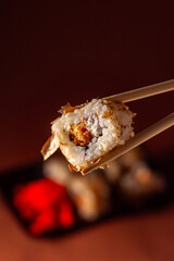 Chopsticks taking portion of sushi roll. Sushi rolls with salmon cream cheese and cucumber in take away package. Food delivery concept.