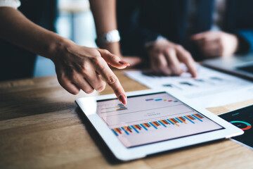 Young businessman and woman in formal sitting in office using tablet working on financial charts in...