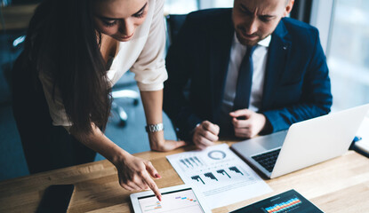 Young businessman and woman in formal sitting in office using tablet working on statistical data of market in workplace in company
