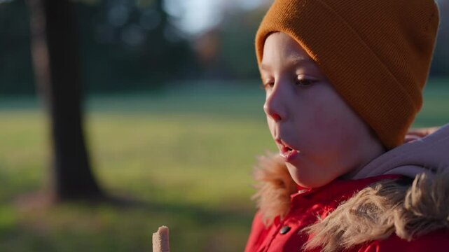 Close-up of a child looking away, chewing a snack, wrapped warmly in a scarf and hat, with a thoughtful expression.