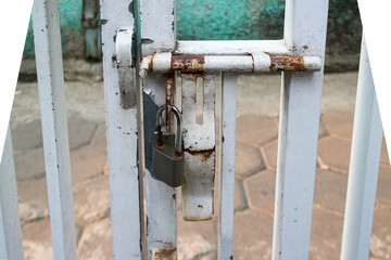 A close-up shot of a rusty lock on a white metal gate. The lock is a classic padlock with a silver finish and appears to be very old. Rusty Lock on a White Steel Gate.