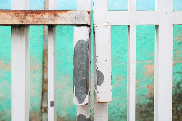 A close-up of an old white metal gate with a rusty metal bar, set against a green wall. A weathered white gate with peeling paint stands against a turquoise wall