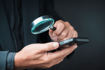 Closeup a man holding a magnifying glass to use with a smartphone in his hand, fact check, and...