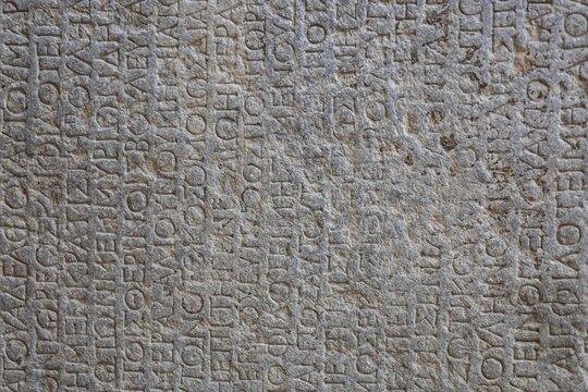 Archaeological Museum of Rhodes, Greece. Travel and history concept. Antique Greek text on stone tablets. Old cuneiform on a stones. Ancient inscription. Gray wall with historic letters.