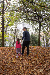 Obraz premium A father and daughter walk hand in hand under an umbrella on a crisp autumn day in a park, surrounded by fallen leaves. A heartwarming moment of connection and exploration in nature.