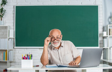 Old male teacher in front of blackboard. Man teacher sitting in front of green board. Portrait...