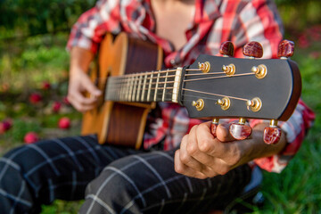 Close up man tuning guitar. Man having fun playing acoustic guitar. Male musician tuning the...