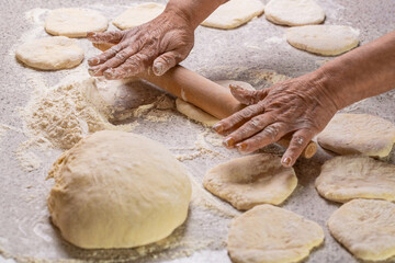 Hands baking bread or pizza dough with rolling pin on table. Woman preparing dough at home. Food preparation, cooking at home, making pizza concept. Woman rolling out dough on kitchen table, closeup