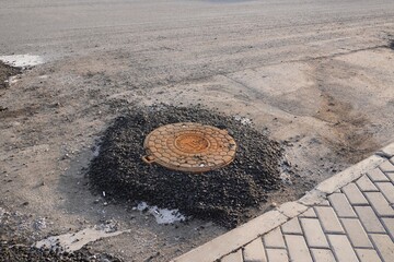 Multiple manhole covers on a street under construction, surrounded by fresh asphalt. 