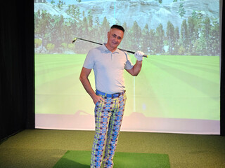 Golfer poses confidently in colorful attire on an indoor driving range with a virtual backdrop