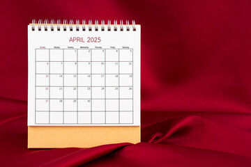 Front view of April 2025 desk calendar on red silk background.