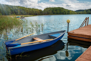 Naklejka premium A blue boat is attached to a wooden pier on a lake with blue water against a mixed forest background