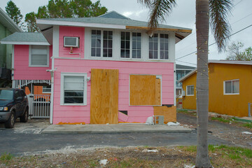 Gulfport, FL, USA. Street view old pink house with plywood on windows, car and palm trees after Hurricane Milton. No people and room for copy. Sunny day.
