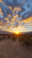 A vibrant orange and blue sunrise over a desert landscape with sand dunes and brush.