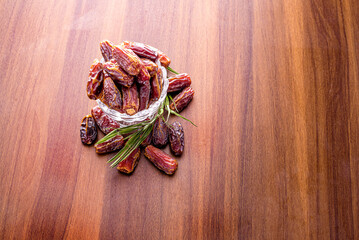 Dried dates in wooden bowl and palm leaves on wooden table.