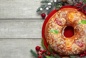 Top view of Roscon de reyes on a red plate with a red berries branches,christmas balls and space...