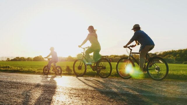 A family rides bicycles along a road at sunset, enjoying an evening in nature