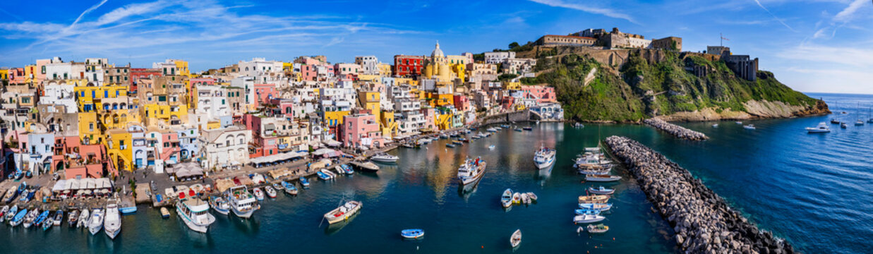 Procida Italy aerial drone view of Corricella port and yellow church. 12k panorama of colorful houses and Terra Murata castle in Gulf of Naples. Authentic Mediterranean island scenery