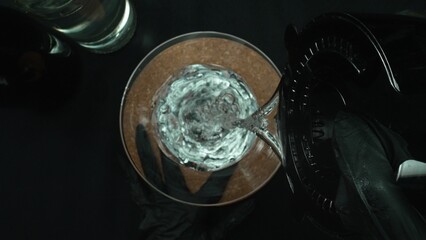 Top down view of skilled bartender hand prepare martini garnished with olive. Close up of hand making transparent cocktail drink with olive with movement and black background. Macrography. Comestible.