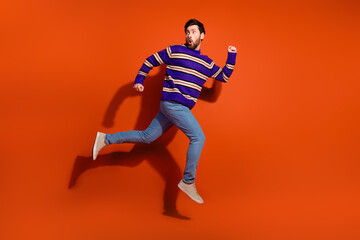 Full length photo of handsome young guy running away fast turn around dressed stylish striped purple garment isolated on orange background