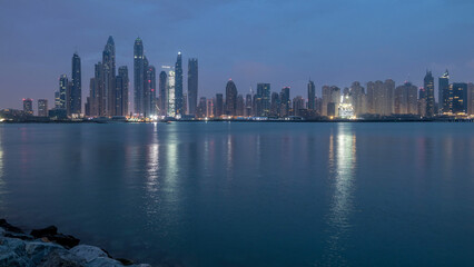 Naklejka premium Panorama of modern skyscrapers in Dubai city night to day timelapse from the Palm Jumeirah Island.