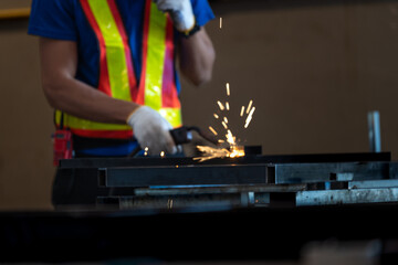 A welder in protective mask and reflective vest operates a welding torch, producing bright sparks in an industrial setting. He wears gloves and a blue shirt, focusing on metalwork with sparks flying.