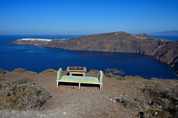 Eine Sitzbank mit Tisch steht am Wanderweg von Fira nach Oia am Wegesrand, und der Blick schweift über das blaue Mittelmeer auf die entfernte Stadt Oia.