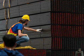 A construction worker in a reflective vest and helmet stands beside stacked metal sheets in an...