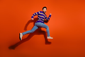 Full size photo of nice young male running fast wear trendy striped violet outfit isolated on orange color background